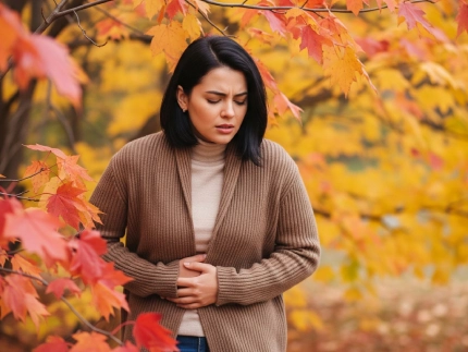 Donna con mal di stomaco tra foglie autunnali, simboleggiando i disturbi digestivi legati al cambio di stagione.
